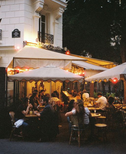 People dining at an outdoor Parisian café terrace at dusk, warm lights glowing