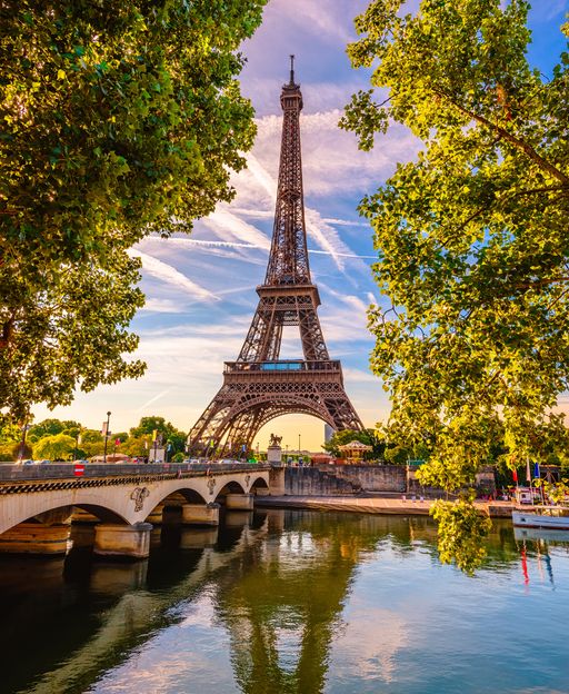 The Eiffel Tower rising above the River Seine in Paris, framed by trees in summer light