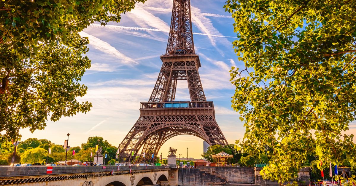 The Eiffel Tower rising above the River Seine in Paris, framed by trees in summer light