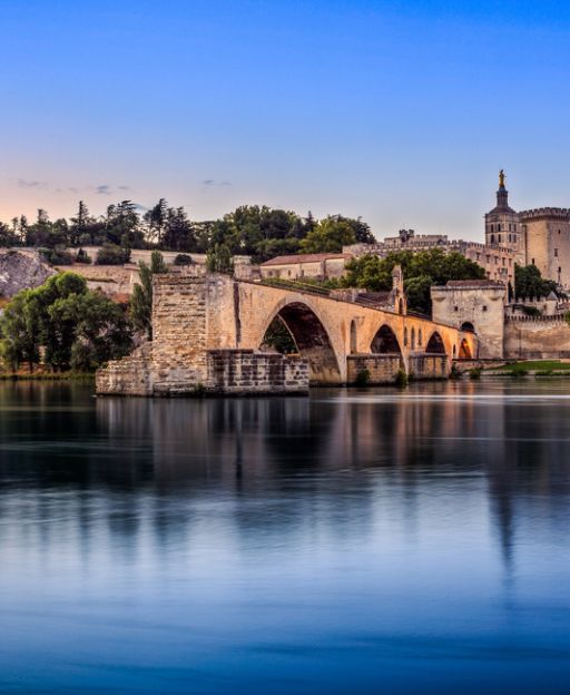 The Pont Saint-Bénézet (Avignon Bridge) reflected in the Rhône river with the Palais des Papes in the background at dawn, Avignon, France