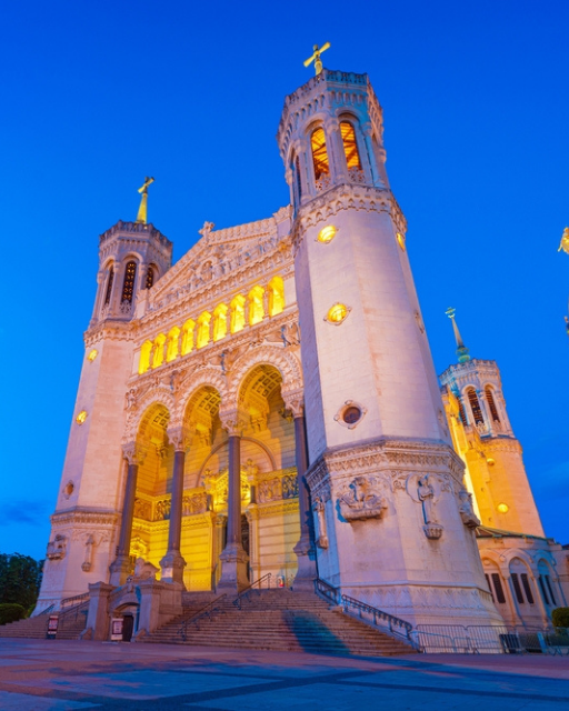 The illuminated Basilica of Notre-Dame de Fourvière in Lyon at dusk, seen against a deep blue sky