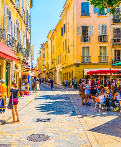Sunny European street with yellow buildings, outdoor cafes, and pedestrians