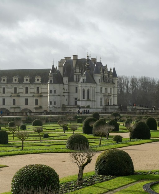 Grand château with ornate towers overlooking manicured formal gardens with topiary
