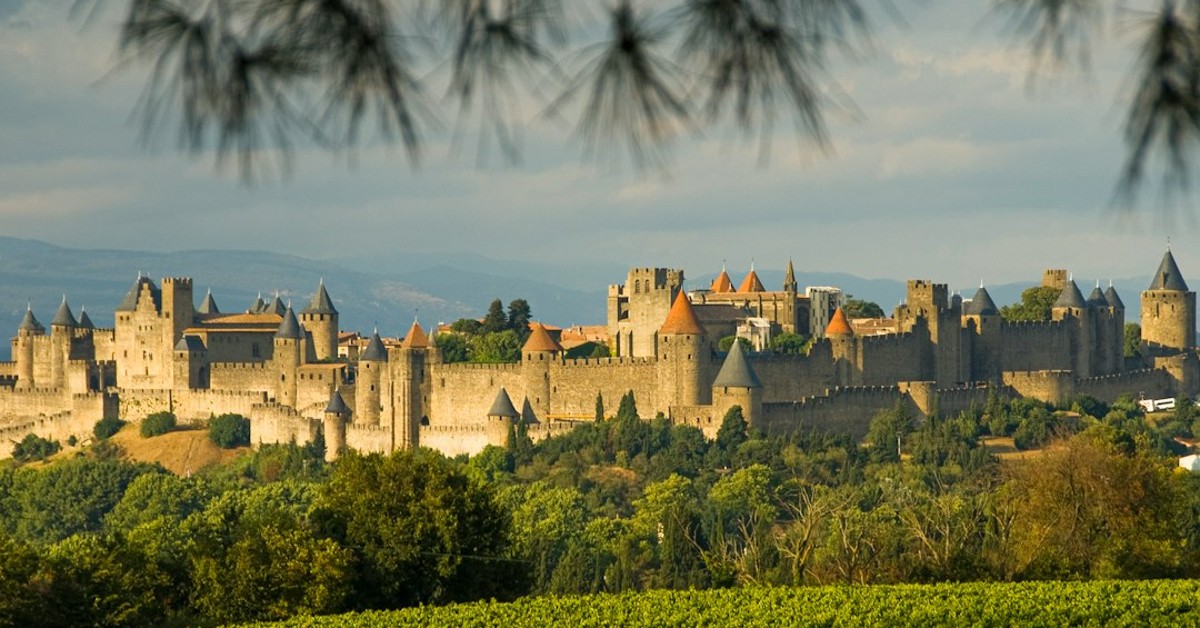 Medieval fortified city with stone towers and walls surrounded by green vegetation under blue sky