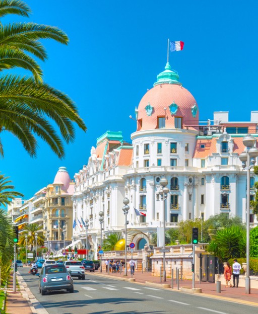 Belle époque hotel with pink dome on Mediterranean promenade lined with palm trees