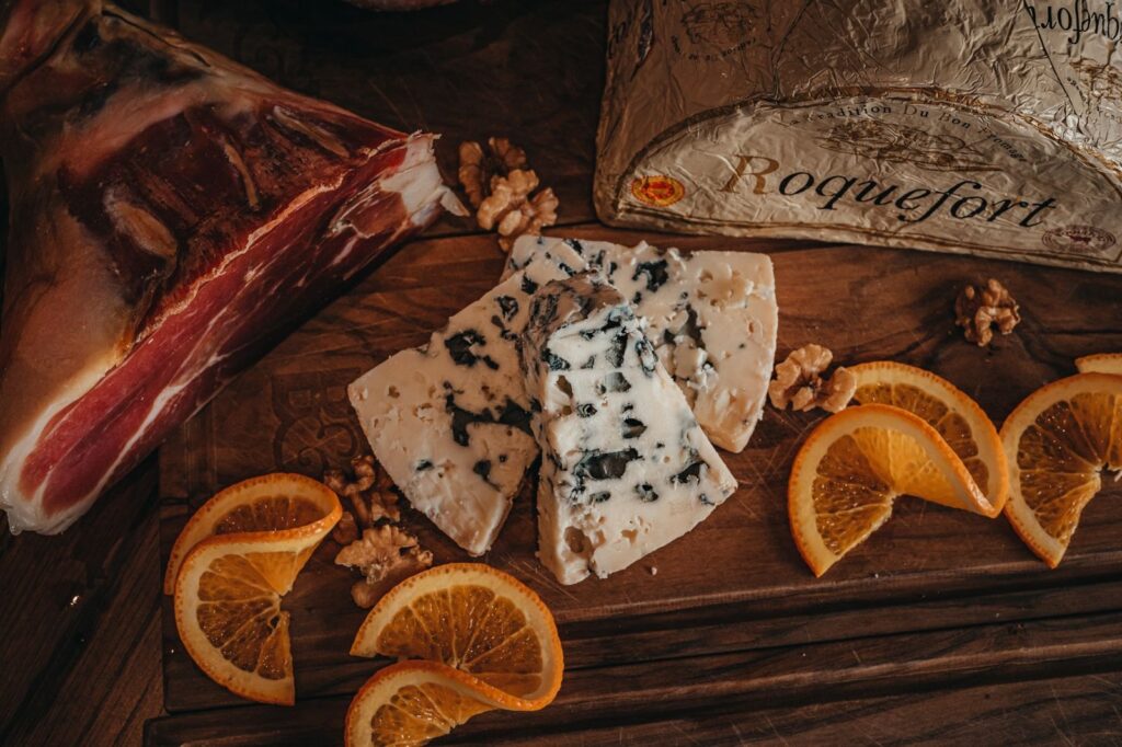Slices of Roquefort blue cheese on a wooden board with orange slices and walnuts